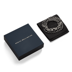 Ellipse Cuban Chain Necklace in graphite, presented coiled on a black display pad next to a signature Daniel Wellington gift box, highlighting its polished Cuban links and elegant packaging.