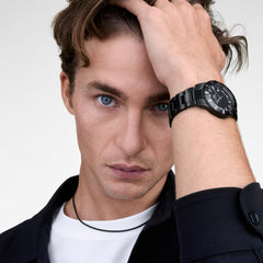 A man wearing the Daniel Wellington Iconic Paradigma Link Black watch, showcasing its sleek black dial, satin matte bezel, and polished 3-link stainless steel bracelet styled with a white T-shirt and dark shirt.