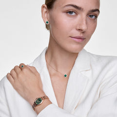 Woman wearing Audrey Earrings Malachite Gold, featuring round green malachite stones bordered by white cubic zirconia crystals, styled with matching gold jewellery and a white blazer for an elegant, coordinated look.