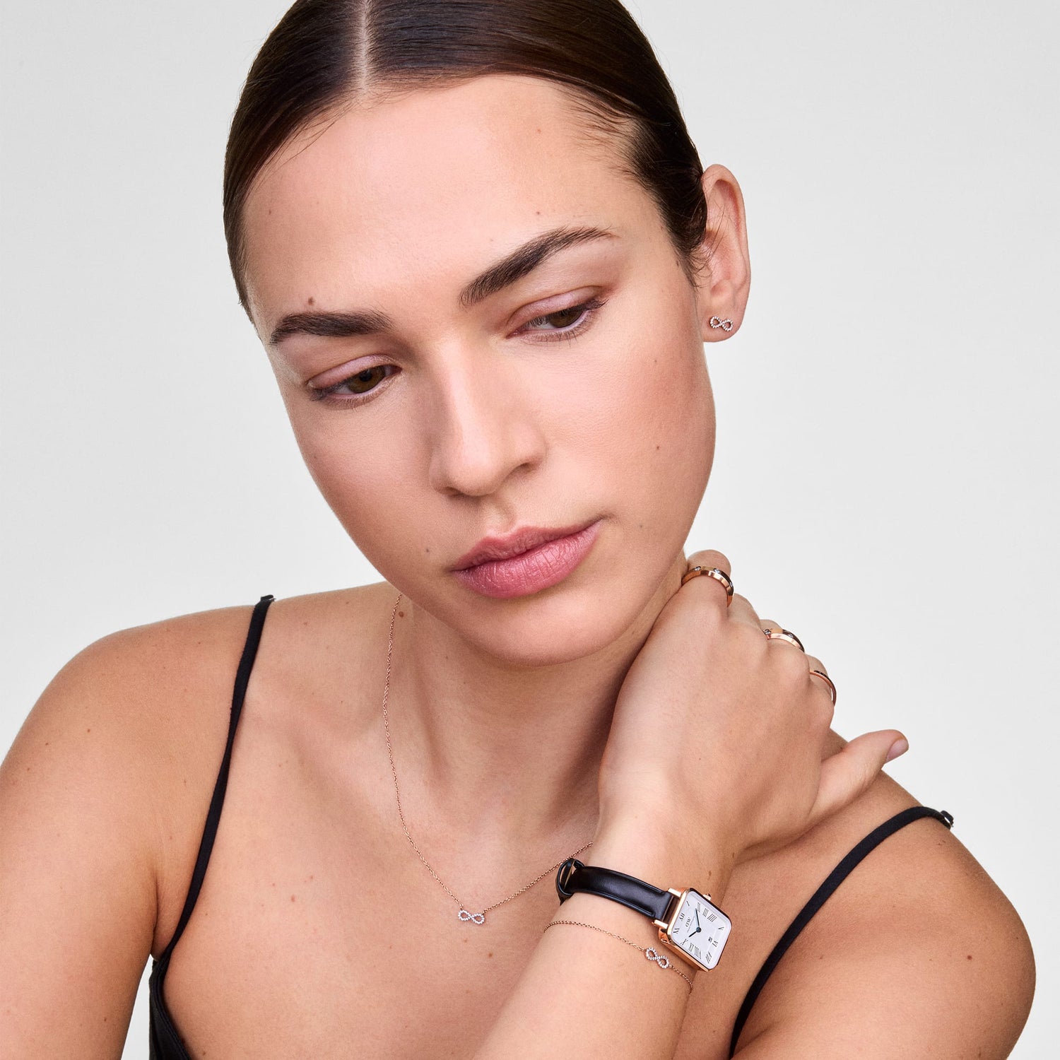 Model wearing Mirelle Infinity Earring Rose Gold, styled with a matching infinity necklace, bracelet, and a rose gold-accented watch, highlighting the delicate pavé set cubic zirconia and minimalist design.
