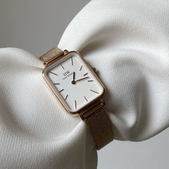 Quadro Pressed Melrose rectangular watch with an eggshell white dial and rose gold mesh strap, elegantly displayed on soft white fabric.