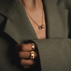 Elan Unity Necklace rose gold with interlocking circles, styled with a blazer and matching rose gold rings for a chic look.