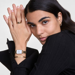 A woman wears the Classic Bracelet Gold by Daniel Wellington on her wrist, styled with a gold watch and black outfit for an elegant, modern look.