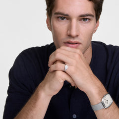 Man wearing a Daniel Wellington rectangular silver watch with a mesh strap and a polished silver mini signet ring, styled with a dark shirt for a refined, modern look.