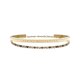 Gold bracelet set featuring a sleek Daniel Wellington engraved cuff paired with a delicate tennis bracelet adorned with honey-toned crystals, both finished in polished gold for an elegant and timeless look.