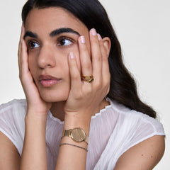 Woman wearing Petite Reflection Gold watch with mesh strap and mirror dial, styled with a delicate bracelet and sheer blouse.