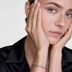 A woman wearing a Classic Tennis Bracelet Honey Combo Gold on her wrist, showcasing the slim gold band with honey-toned Preciosa crystals styled elegantly with a black blouse.