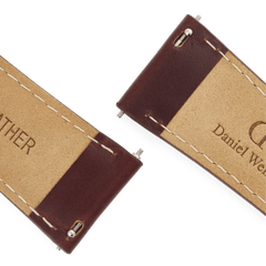Close-up of the underside of the Tapered St Mawes Strap Gold, showing genuine brown leather with cream contrast stitching and quick-release spring bars for easy attachment. The Daniel Wellington branding is clearly visible, highlighting the quality craftsmanship of the watch strap.