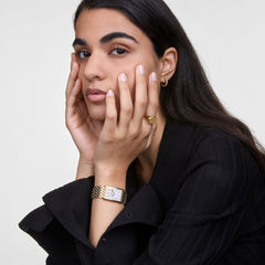 Woman wearing a gold signet ring on her little finger, styled with a black blazer and gold watch for a modern, elegant look.