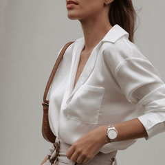 Woman wearing the Daniel Wellington Iconic Link Lumine watch with a silver and rose gold bracelet and crystal-set white dial, styled with a crisp white blouse and neutral accessories for a refined daytime look.