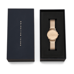 Petite Reflection Rose Gold women’s watch with a mirror glass dial and rose gold mesh strap, elegantly presented in a black Daniel Wellington gift box.