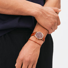 A person wearing the St Mawes Bracelet Rose Gold, styled with a matching brown leather watch, showcasing its slim and elegant design on the wrist.