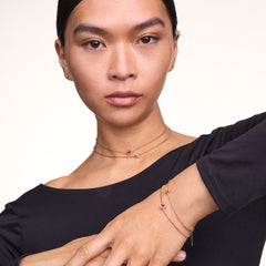 Model wearing the July Charm Gold, featuring a vivid red crystal set in gold-plated stainless steel, styled on a delicate necklace and bracelet for an elegant, modern look.