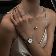 Woman wearing the Daniel Wellington Iconic Link Lumine watch with a two-tone silver and rose gold bracelet and crystal-set white dial, styled with a satin dress and silver jewellery for an elegant evening look.