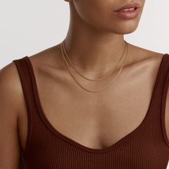 A woman wearing the Box Chain Necklace G in gold, styled as a delicate, layered accessory with a minimalist look against a brown ribbed top.