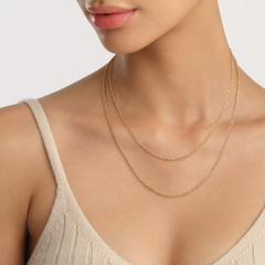 A woman wears the Twisted Chain Necklace G, featuring a delicate gold rope-inspired design, layered elegantly over a neutral knit top.