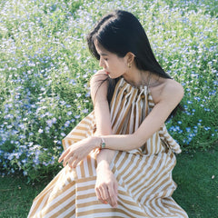 Woman wearing Quadro Mini Evergold Emerald gold watch with emerald green dial, styled outdoors in a striped summer dress.