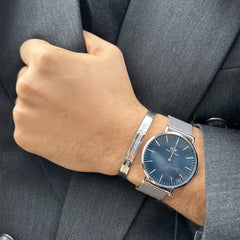 A Daniel Wellington Elan Bracelet Silver styled on a wrist alongside a silver mesh strap watch, paired with a tailored grey suit for a refined, modern look.