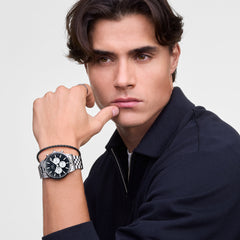 A person wearing the Daniel Braided Leather Bracelet Sheffield 2.8 Silver on their wrist, styled alongside a stainless steel watch for a modern, coordinated look. The slim black braided leather band and polished silver clasp offer a refined, minimalist accent suitable for both casual and formal outfits.
