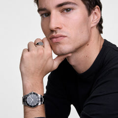 Man wearing the Daniel Wellington Iconic Paradigma Black watch with a silver link strap and a classic silver signet ring, styled with a black jumper for a modern, sophisticated look.
