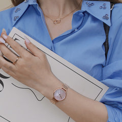 Woman wearing the Petite Lumine 5 Link Melrose Pink MoP Rose Gold watch, styled with a blue shirt and rose gold jewellery, highlighting the pink mother of pearl dial and crystal hour markers.