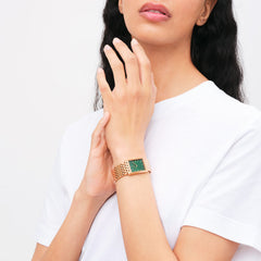 A woman wearing the Bound 9-Link Emerald Sunray watch, featuring a rectangular rose gold case, 9-link bracelet, and striking emerald green dial, styled with a white top.