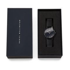 Daniel Wellington Petite Reflection Black watch with a mirror glass dial and black mesh strap, elegantly presented in a branded gift box.