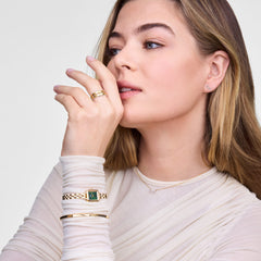 A woman wears the Mirelle Infinity Earring Gold, showcasing the delicate gold infinity stud with sparkling white cubic zirconia crystals, styled with a gold watch, bracelets, and rings for an elegant, coordinated look.
