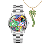 Limited edition Daniel Wellington watch with a silver steel link strap and a multicolour Steven Harrington art dial, paired with a gold necklace featuring a playful green palm tree charm.
