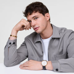 A man wearing the Classic Bangle Gold by Daniel Wellington on his wrist, styled with a grey shirt and paired with a classic gold and black watch for a refined, modern look.