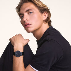 A man wearing the Classic Piano Link Graphite Unitone watch, showing its brushed graphite dial and matching piano link strap styled with a casual dark t-shirt.