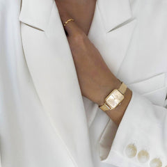 Quadro Pressed Unitone Gold women’s watch with rectangular dial and mesh strap, styled with an elegant white blazer.