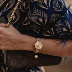 Woman wearing the Petite Unitone rose gold watch with a minimalist dial and mesh strap, styled with a patterned blouse and a designer handbag.