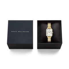 Daniel Wellington Quadro Roman Numerals Date 5-link Gold watch presented in a black gift box, showcasing its rectangular gold case, white dial with Roman numerals, and polished gold bracelet.