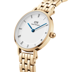 Close-up of petite gold 5-link women’s watch with white Roman numeral dial and blue hands, Daniel Wellington branding.