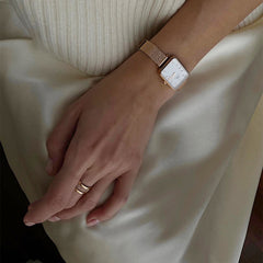 A hand wearing the Elan Dual Ring Rose Gold with a matching rose gold mesh strap watch, styled against a cream satin skirt and ribbed knit top.
