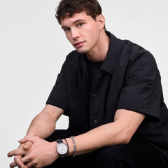 Man wearing the Classic Multi-Eye Sheffield Off-white Sunray Silver watch with a black leather strap, styled with a silver bracelet and short-sleeved black shirt for a modern, understated look. The watch’s off-white sunray dial and minimalist silver case add a refined touch to the casual outfit.