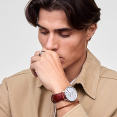 A person wearing the Daniel Braided Leather Bracelet St Mawes 2.8 Silver, featuring a slim brown braided leather band with a polished silver clasp, styled alongside a classic brown leather strap watch for a refined, layered look.