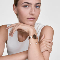 Woman wearing the Petite Reflection Rose Gold watch, featuring a mirror glass dial and rose gold mesh strap, styled with a delicate bracelet for an elegant, modern look.