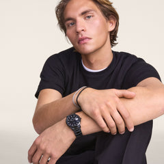 Man wearing the Daniel Wellington Iconic Link Automatic Black watch with a black enamel dial and stainless steel bracelet, styled casually with a black t-shirt.