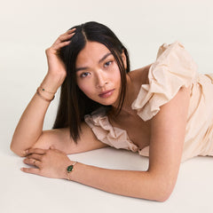 A woman wearing the May Charm Gold on a delicate bracelet, styled with a soft neutral outfit and layered gold jewellery for an elegant, modern look.