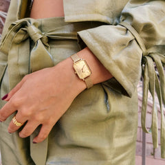 Woman wearing Quadro Pressed Unitone Gold watch with rectangular gold dial and mesh strap, styled with a sage green outfit.