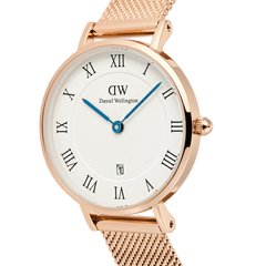 Close-up of the Petite Roman Numerals Date Rose Gold watch, showcasing its polished rose gold case, crisp white dial with black Roman numerals, blue hands, and a date window at six o’clock. The fine mesh bracelet and guilloché pattern add a refined, elegant touch.