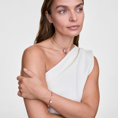 Woman wearing the Amethyst Octagon Rose Gold Charm on a delicate necklace and matching bracelet, styled with a white one-shoulder top for an elegant, modern look. The purple amethyst charms add a subtle pop of colour to her layered jewellery.