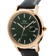Close-up of the Daniel Wellington Iconic Sheffield Automatic Rose Gold watch, showing its emerald green enamel dial, rose gold case, magnified date window, and black leather strap.