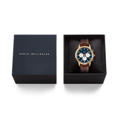 Daniel Wellington Iconic Chronograph St Mawes Arctic Panda Gold watch with a blue dial and brown leather strap, presented in an elegant black gift box with gold branding.