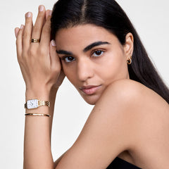 Woman wearing a Daniel Wellington Quadro Roman Numerals 5-Link Gold watch with rectangular dial and gold bracelet strap.