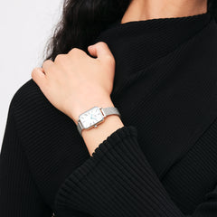 Woman wearing Quadro Roman Numerals Sterling watch with silver mesh strap and white rectangular dial, styled with black knit.