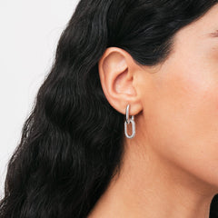 A woman wearing a Crystal Link Earring in silver, featuring a polished oval link encrusted with sparkling cubic zirconia crystals for a modern, elegant look.