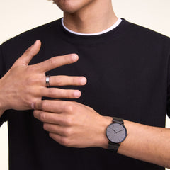 A man wearing the Classic Piano Link Onyx Unitone watch with a brushed black dial and stainless steel piano link strap, styled with a black t-shirt for a modern, understated look.